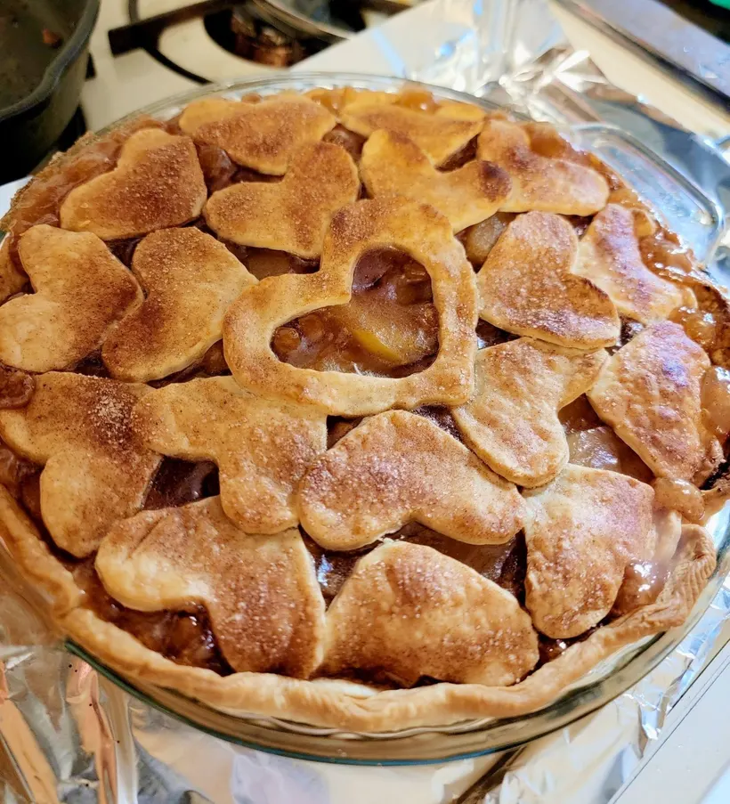Apple pie with heart-shaped crust cutouts photographed on a kitchen counter beside foil